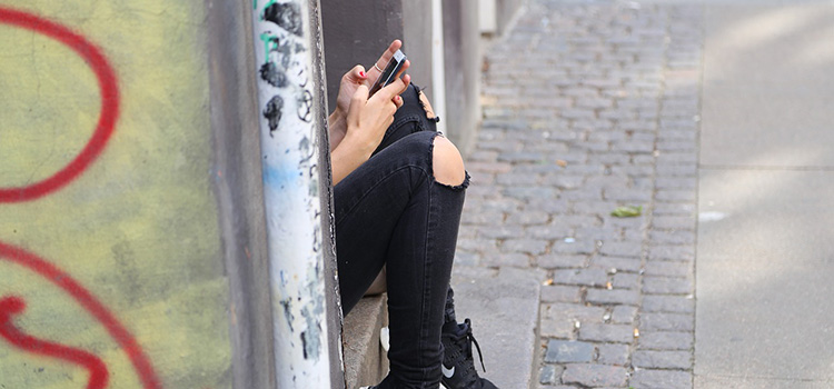 Ungdom med mobiltelefon på trottoar
