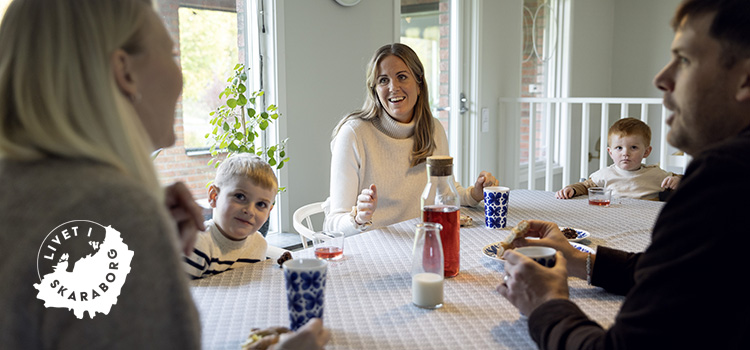 Vuxna och barn sitter och fikar, Logotyp Livet i Skaraborg