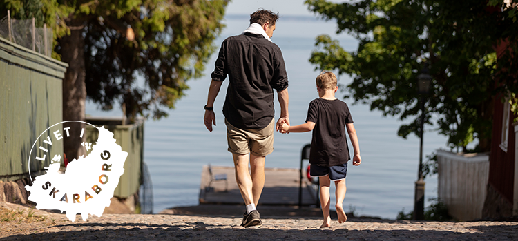 Pappa och son går längst kullerstensgata mot sjö